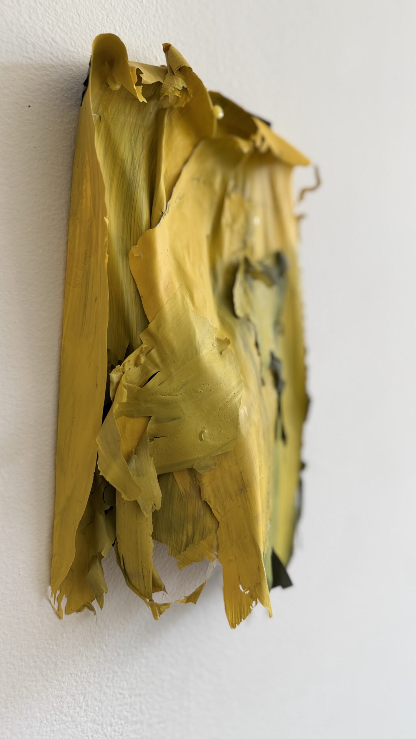 Detalle de una obra de Gabriela Sánchez con capas amarillas levantadas y pliegues sobre una pared blanca.